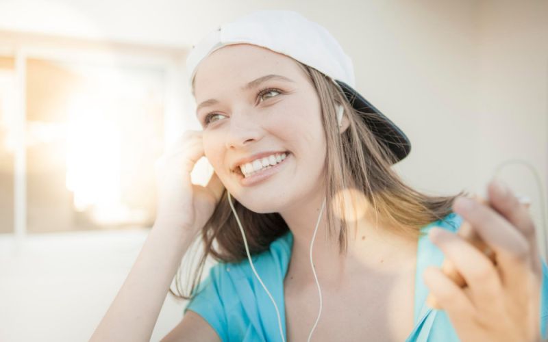 A woman in a hat enjoying music through headphones, smiling and immersed in her listening experience.