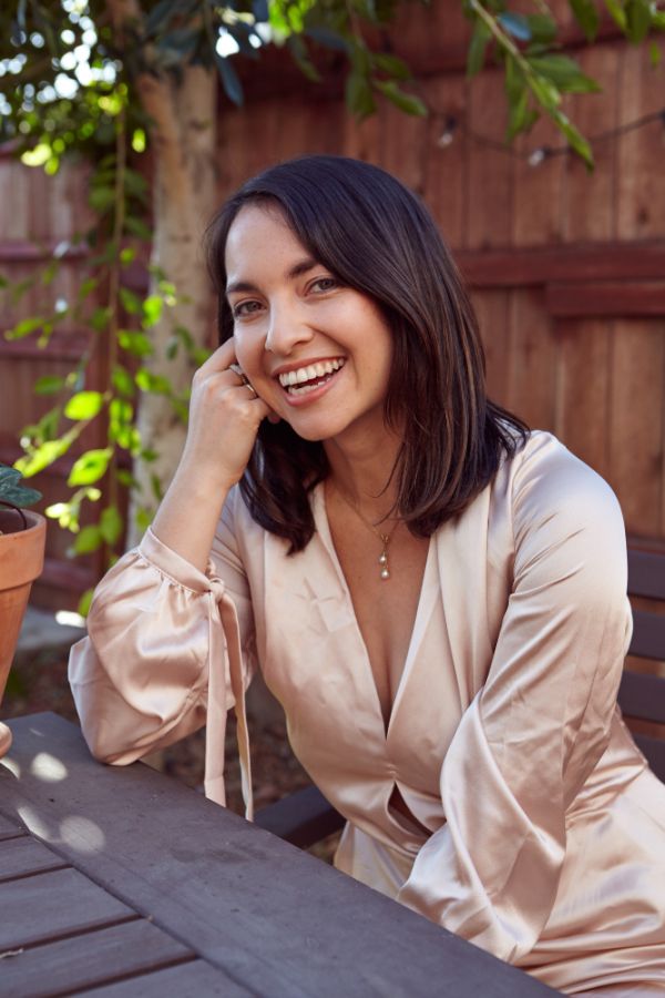 woman sitting in the garden her arm is on the table with her hand touching her hair, depicting fixed dental implants
