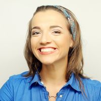 A woman wearing a blue shirt and a headband, showcasing her Invisalign aligners with a confident smile