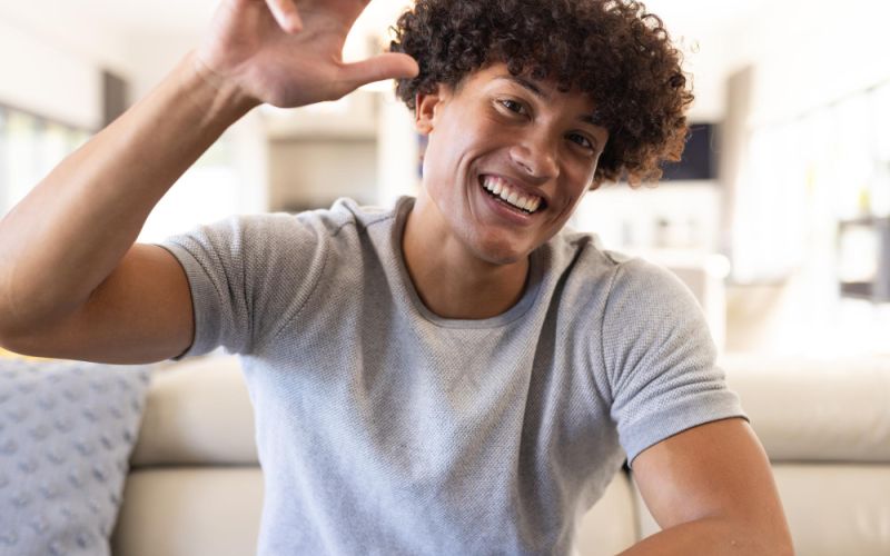 A man with curly hair is seated on a couch, appearing calm and at ease in a cozy living room setting.